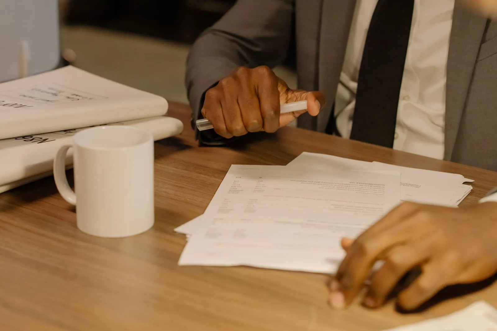 Mãos carimbando documentos da empresa sobre uma mesa de madeira, ao lado de uma caneca