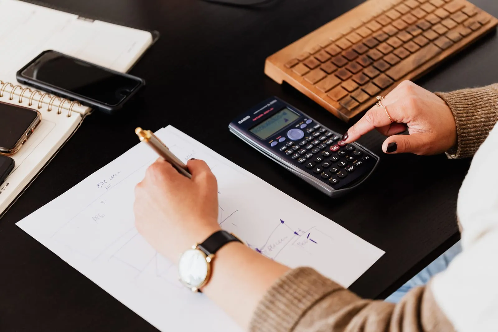 Mãos fazendo contas na calculadora e anotando em uma folha sobre a mesa do escritório