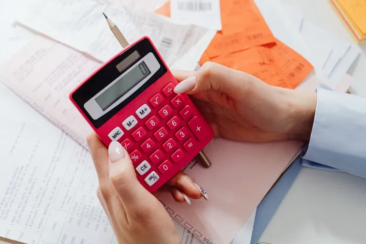 Mãos seguram uma calculadora vermelha sobre notas e recibos da empresa