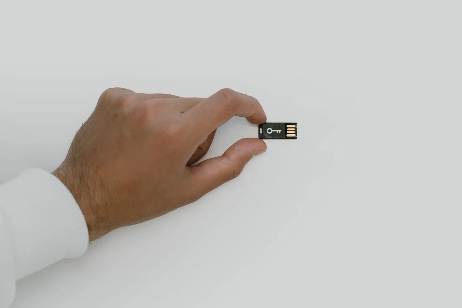 Mão segurando um pequeno token USB de certificado digital sobre fundo claro