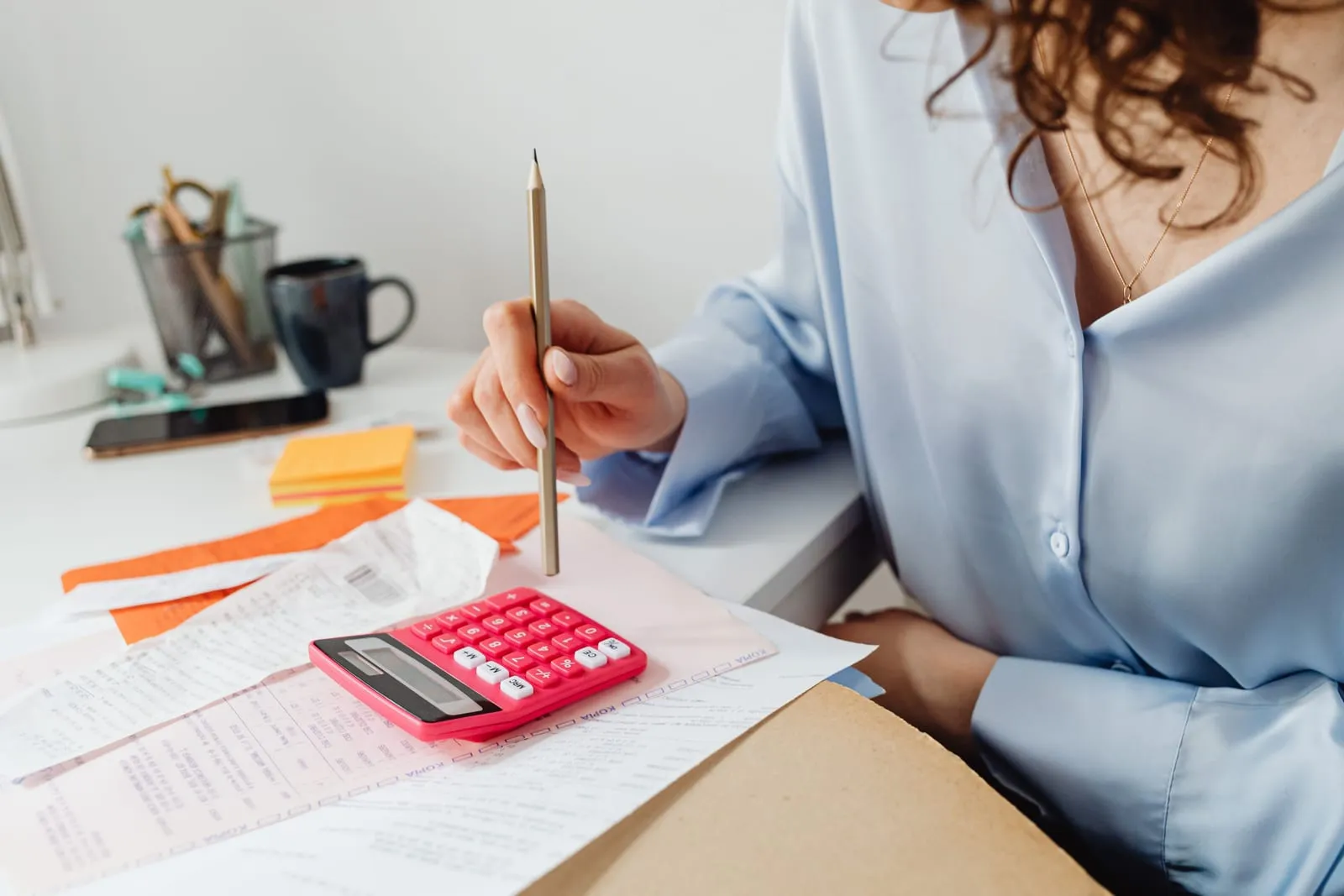 Pessoa com lápis na mão conferindo contas e recibos ao lado de uma calculadora